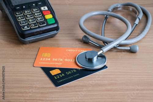 Electronic payment terminal with credit cards and stethoscope on wooden desk. Perfect for health insurance, hospital payment systems, healthcare costs, medical finance articles, and fintech healthcare