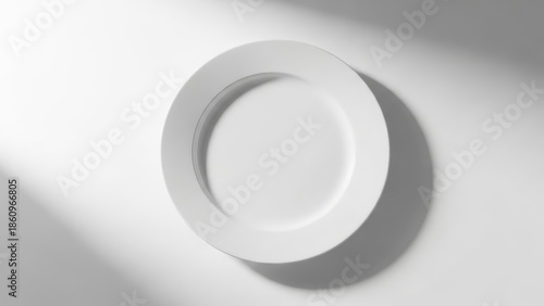 Minimalist empty white plate on a bright white background with soft, abstract light and shadow patterns, perfect for copy space or mockups.