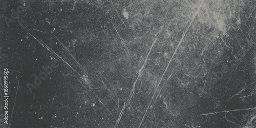 A grayscale image depicts a dark textured surface with scattered light streaks and subtle imperfections throughout