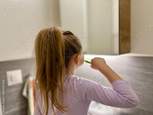 Little blonde girl brushes her teeth and looks in the mirror