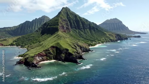 Aerial view of a lush green mountain range meeting the coast, with a clear turquoise ocean and white sand beaches