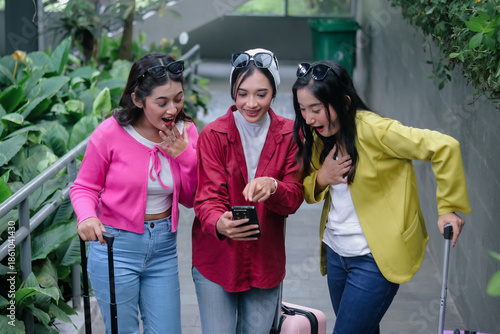 Three overjoyed friends view captivating flight details on a smartphone, expressing visible delight as they eagerly anticipate their trip. This moment encapsulates sheer excitement and connection.