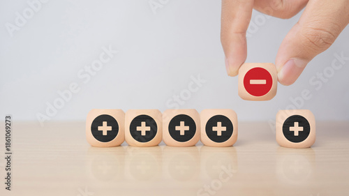Hand removing a minus symbol from a row of plus icons on wooden blocks, symbolizing problem solving, correction, decision making, and eliminating negative factors.