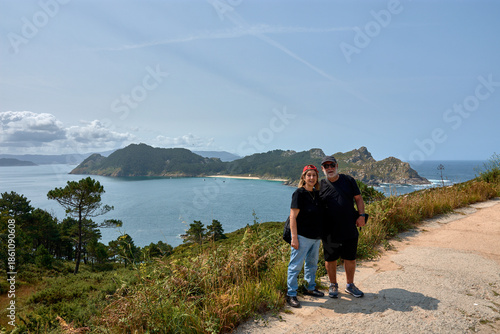 Happy senior couple with visors smiling in front of Cies Islands' beauty.