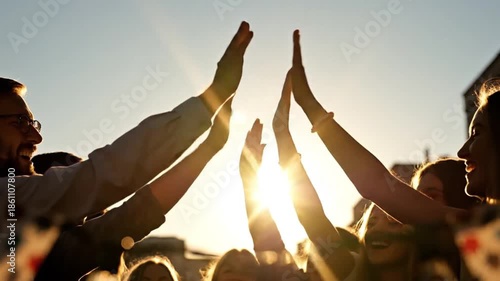 Joyful group high-fiving in warm sunset light, symbolizing teamwork, achievement, and collaboration against a vibrant sky backdrop.
