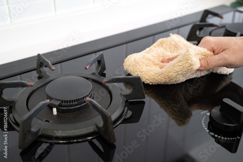 Hand wiping black gas stove burner with cloth during home spring cleaning
