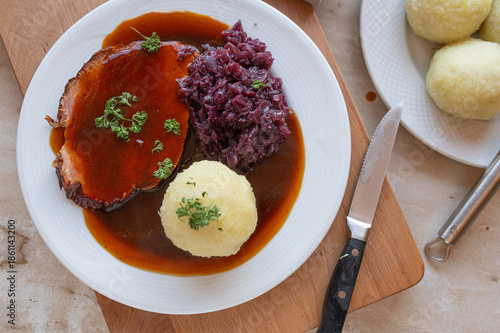 Delicious homemade roast pork with red cabbage, potato dumpling and gravy on a plate. Traditional german food