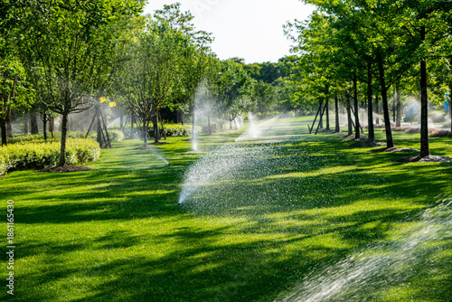 an automatic irrigation system watering a lush green garden. The scene is brightly lit by the sun, with water droplets visible in the air