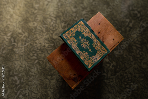 Green covered book with ornate gold details resting on a wooden stand, top view with patterned carpet background and calm spiritual mood