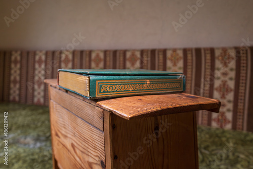 Green hardcover book with gold detailing placed on a wooden stand in a traditional interior, shallow depth of field and calm atmosphere