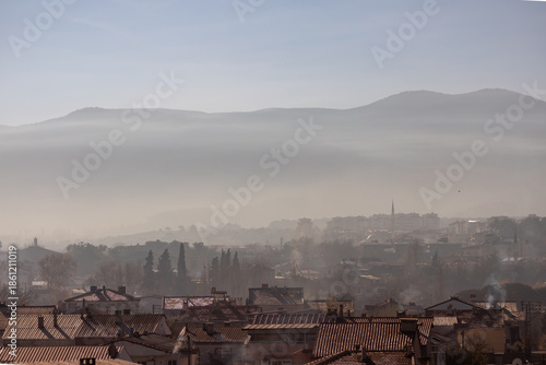 Misty town view in Canakkale Turkey with mosque minaret and rooftops at sunrise, surrounded by hills and soft morning fog