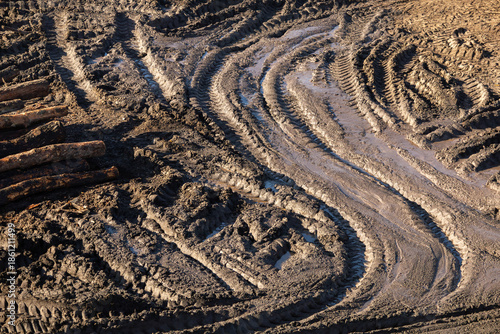 Deep tire tracks in muddy ground with wet soil texture, showing heavy machinery movement and rugged outdoor terrain