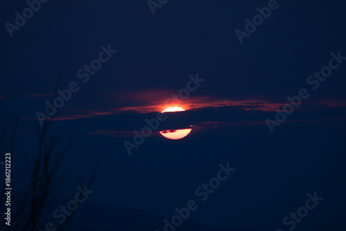 Dramatic sunset with the sun partially hidden by dark clouds, creating a moody sky and minimal atmospheric landscape