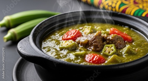 Vibrant Ivorian Sauce Gombo - Slimy Okra Stew with Beef in Traditional Black Clay Pot featuring Senufo Textile and Copy Space