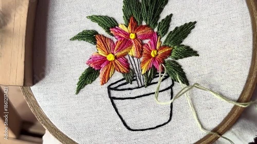 Close up of artist hands embroidering colorful flowers in a pot on white fabric with needle and thread