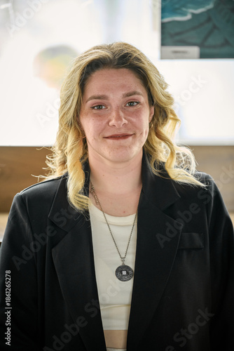Young woman with blonde hair in black blazer smiling indoors with natural light