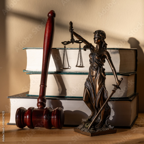 A figure of Themis, books and a judge's gavel against a wall in sunlight
