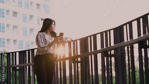Young woman using smartphone standing in front of a office building outdoors during sunset.