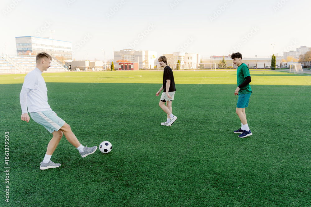 Obraz premium Three young boys play soccer on a lush green field under clear skies. They share laughter and fun while practicing their skills, creating joyful memories together.