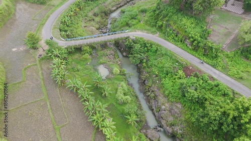 Beautiful aerial view of a winding road crossing a small bridge through green rice terraces.