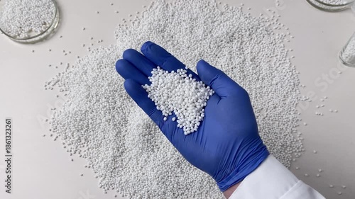A laboratory technician in blue gloves checks the quality of a batch of white thermoplastic granules. Plastic granules are a raw material for industry.