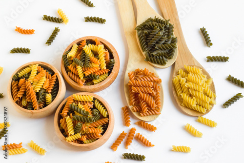 Turkish colorful spiral pasta with tomatoes and spinach was designed in a bamboo bowlson white surface with wooden spoons