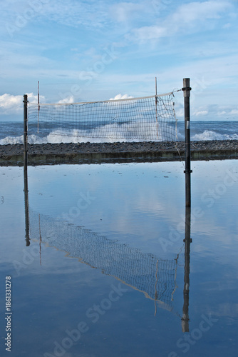 Beach Volleyball Net Standing in Floodwater with Blue Sky Reflection After Storm