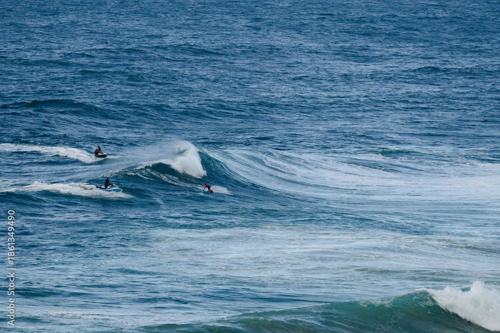 Fototapeta premium Surfers ride large ocean waves in a vibrant blue sea, capturing action and teamwork