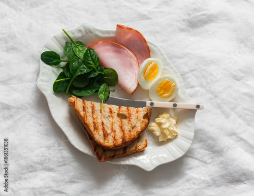 Delicious breakfast, brunch - grilled bread, boiled egg, spinach, ham on a light background, top view