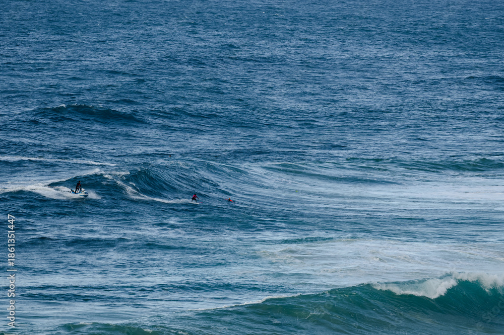 Fototapeta premium Surfers riding large ocean waves together, distant riders in turquoise sea