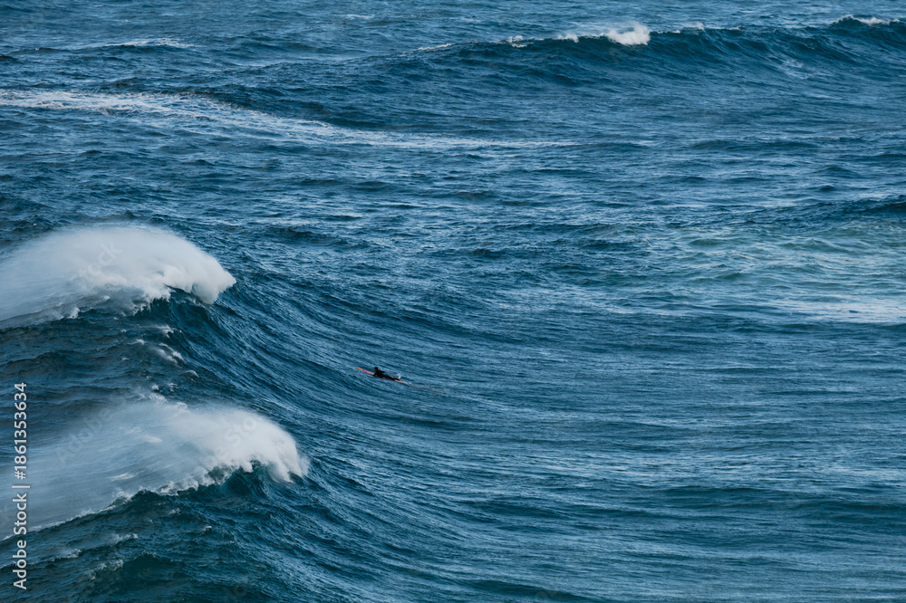 Fototapeta premium A lone surfer rides a massive blue ocean wave under a clear sky