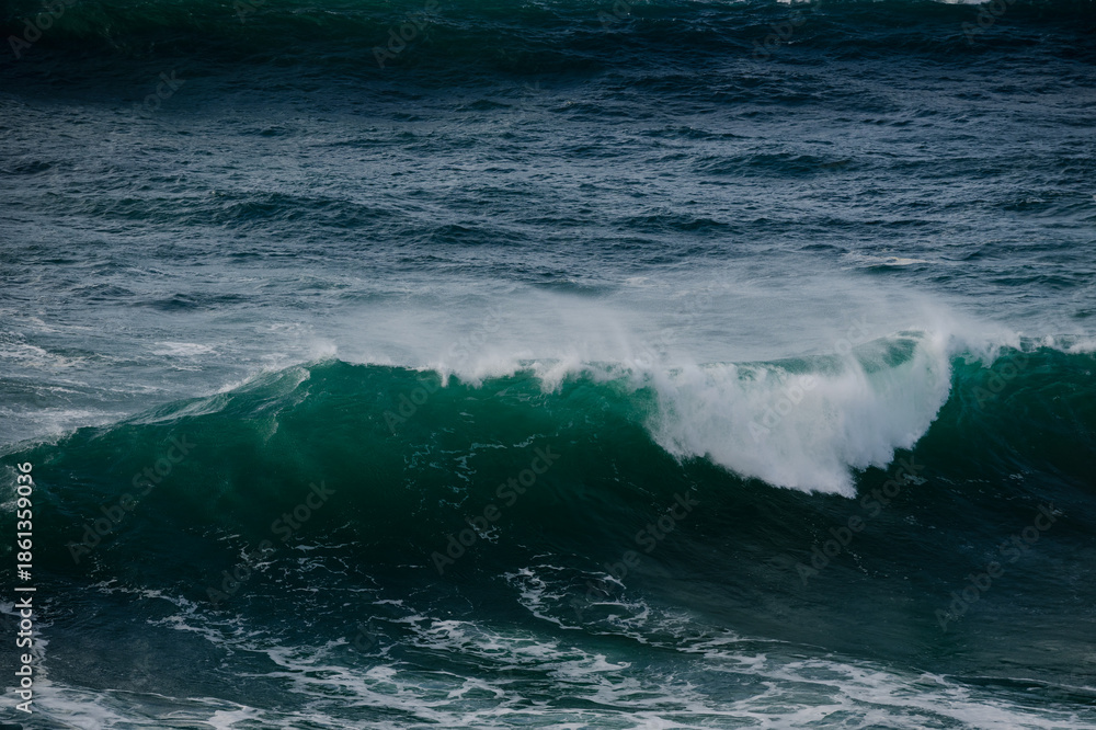 Naklejka premium Majestic ocean wave cresting with deep blue-green water and white spray, dramatic seascape