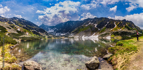 Stunning view of Nizne Temnosmrecinske pleso, a glacial lake in the High Tatras National Park, Slovakia. The image features transparent water with rocks on the bottom, surrounding jagged mountain peak