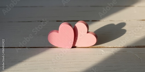 Two pink wooden hearts on rustic white table bathed in sunlight