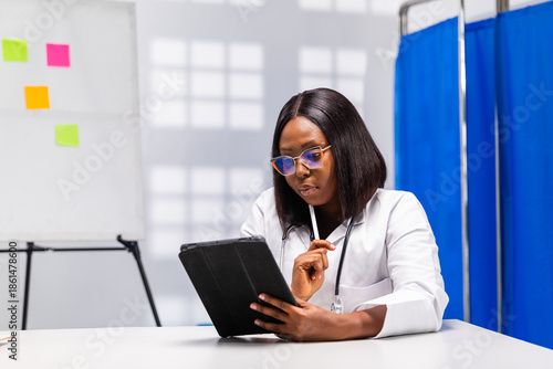 Billede på lærred African female doctor reviews medical information on a smart tablet in a hospita