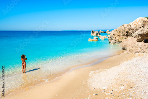 Wallpaper Mural Unidentified young woman in swimsuit taking picture of amazing Megali Petra beach with turquoise sea and rocks, Lefkada island, Greece Torontodigital.ca