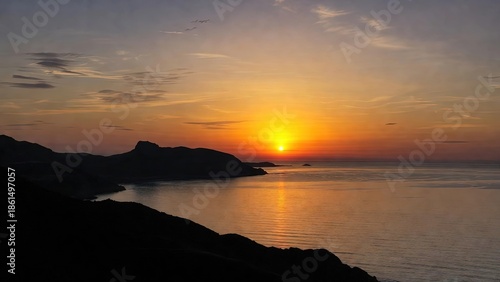 Golden sunset over calm sea with dark coastal land silhouettes