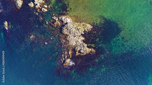 Golden light paints the rocky shore as calm waves softly kiss the surface of the water, capturing a moment of serenity at dawn along the coast.