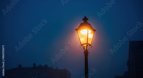 A solitary illuminated street lamp casts a warm glow against a dark, foggy blue sky