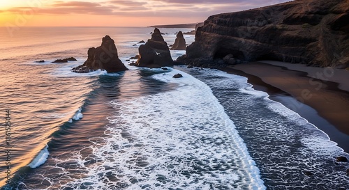 Aerial view of a coastline at sunset, waves crashing on a black sand beach with rock formations and cliffs. Dramatic sky adds vibrancy