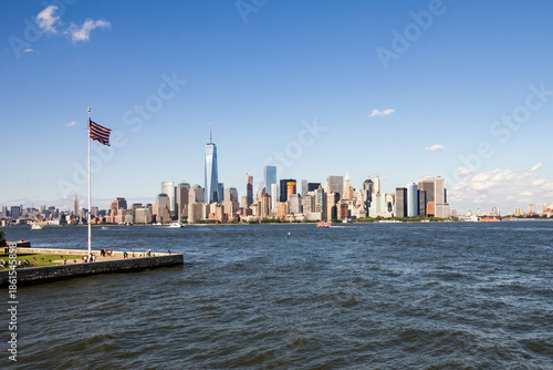 Quadro su tela Flag of America fluttering in the breeze on Ellis Island with New York unmistake