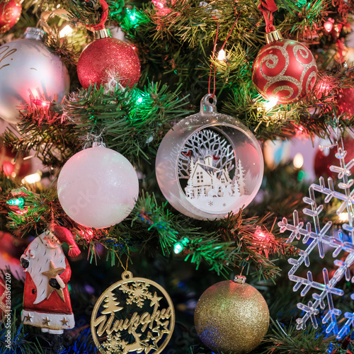 Close-up view of decorated Christmas tree with red, white, and glass ornaments illuminated by colorful festive lights. Traditional holiday decoration with warm atmosphere, shallow depth of field, and 
