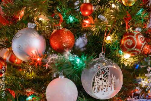 Close-up view of decorated Christmas tree with red, white, and glass ornaments illuminated by colorful festive lights. Traditional holiday decoration with warm atmosphere, shallow depth of field, and 