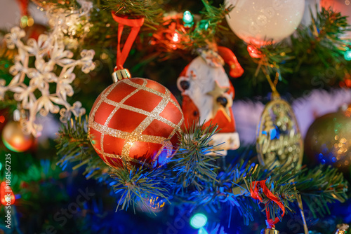 Close-up view of decorated Christmas tree with red, white, and glass ornaments illuminated by colorful festive lights. Traditional holiday decoration with warm atmosphere, shallow depth of field, and 