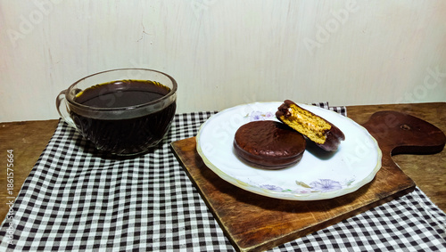 A cozy snack time arrangement featuring chocolate treats and coffee on a checkered napkin and wooden surface.