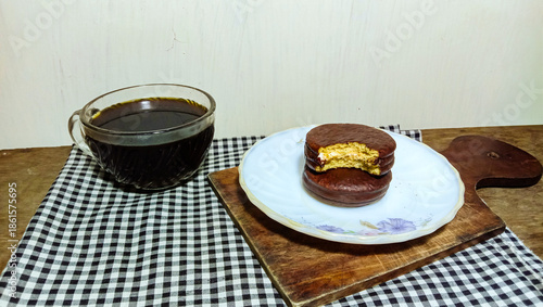 Eye-level shot of chocolate marshmallow pies and a cup of black coffee on a rustic wooden table.