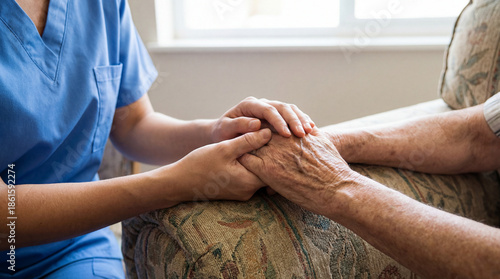 A caregiver in blue scrubs gently holding the hands of an elderly person, offering comfort and support in a home setting.