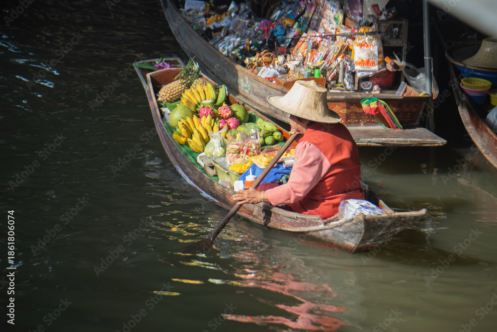 Obraz premium Local fruit vendor rowing a boat at a traditional Thai floating market.