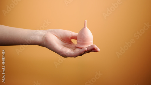 Female Hand Holding Menstrual Cup on Orange Background Minimal Hygiene