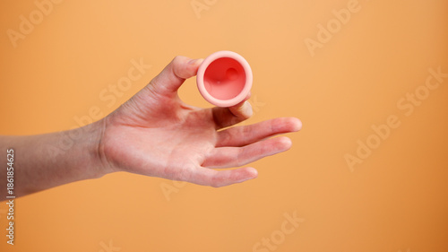 Female Hand Holding Menstrual Cup on Orange Background Minimal Hygiene